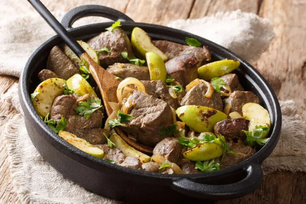 Cooked beef liver with sliced green apples, onions and herbs in a skillet.