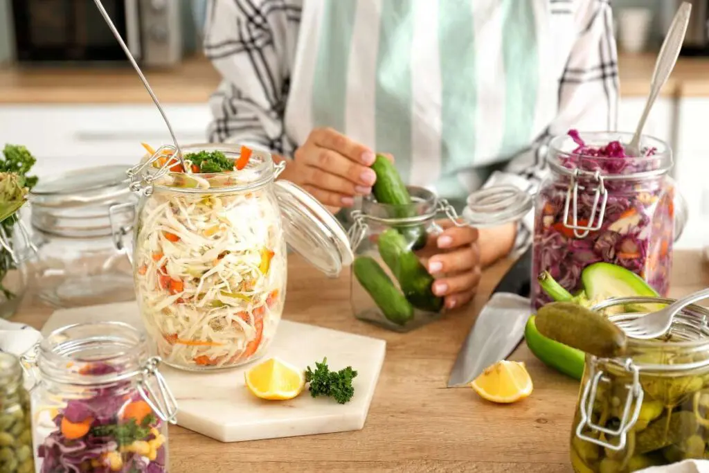 Woman preparing cucumbers for fermentation along with other fermented foods at the table.