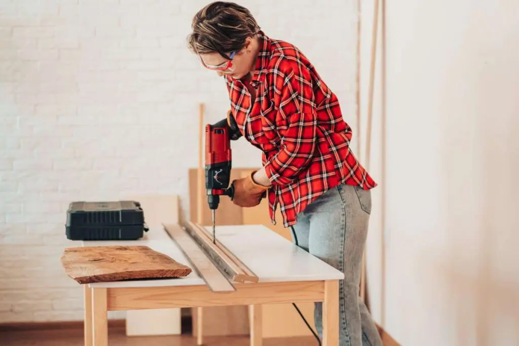 A girl drilling plank with drill on the table.