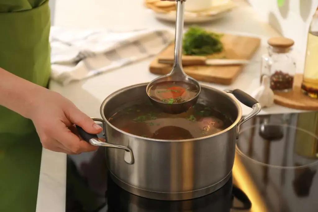 Woman making bouillon on stove in kitchen.