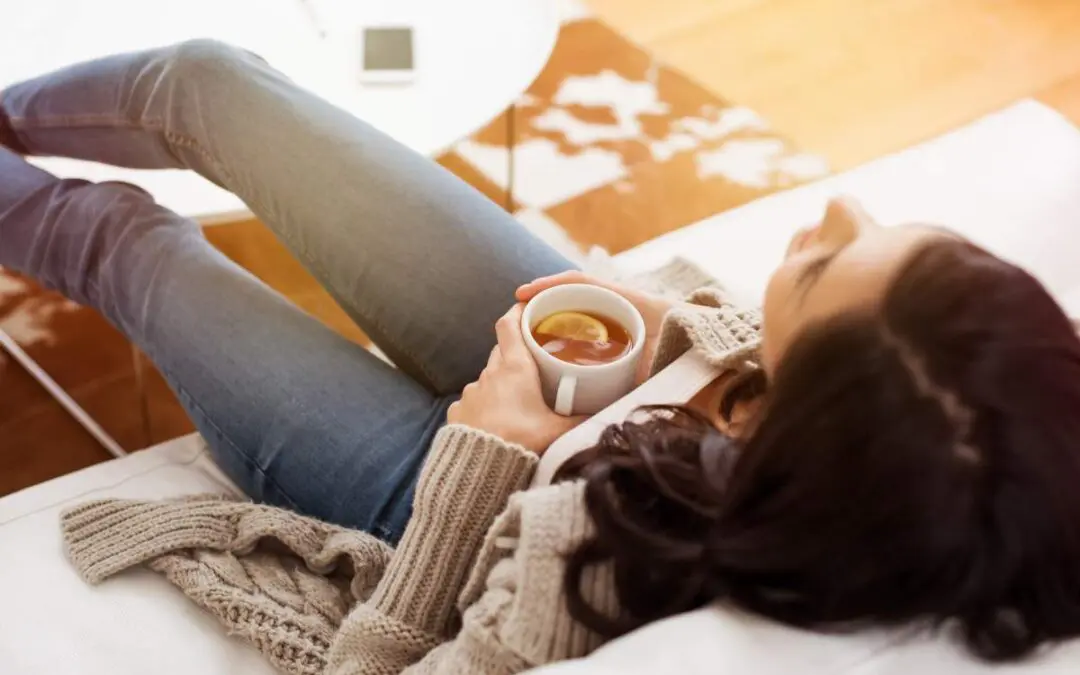 A girl sitting on the couch with her feet up while holding a cup of tea.