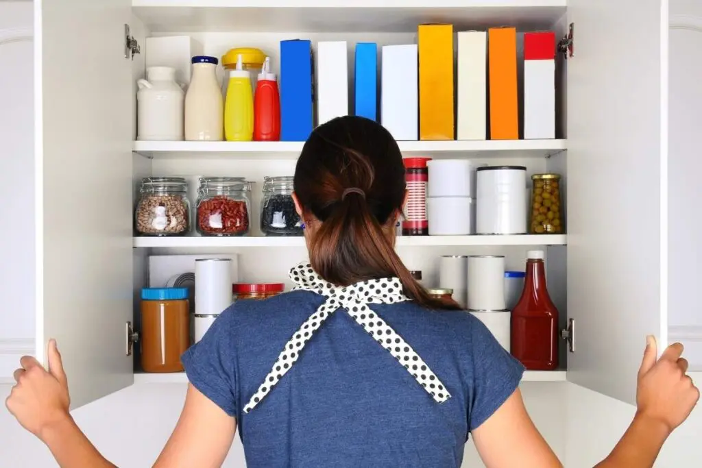 A woman looks into a pantry filled with jars, bottles, and boxes.