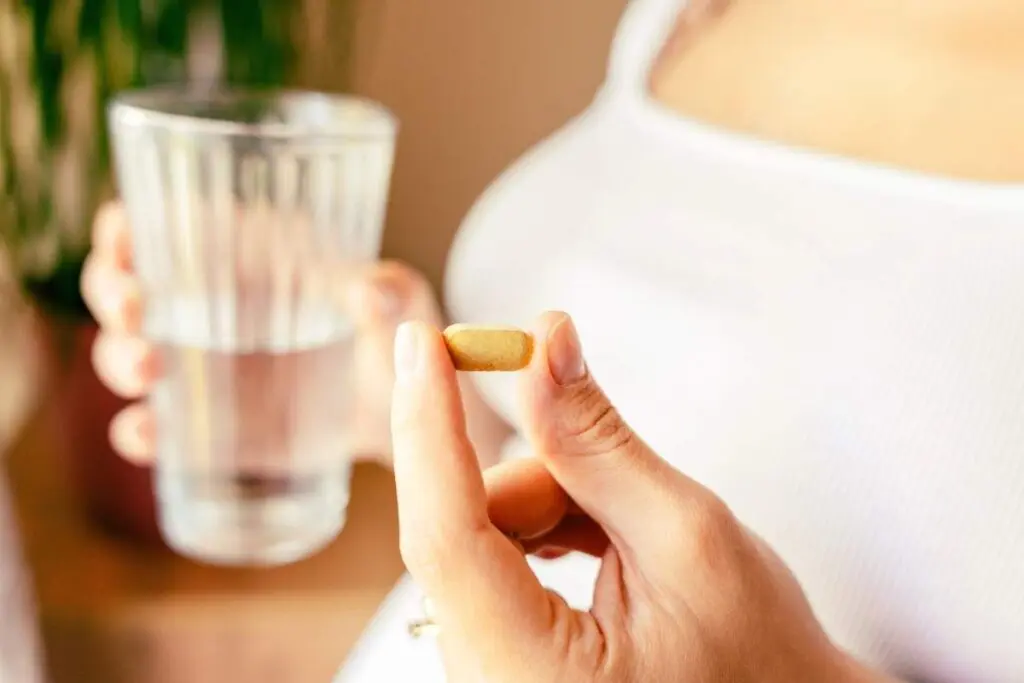 A person holding a yellow pill in one hand and a glass of water in the other.