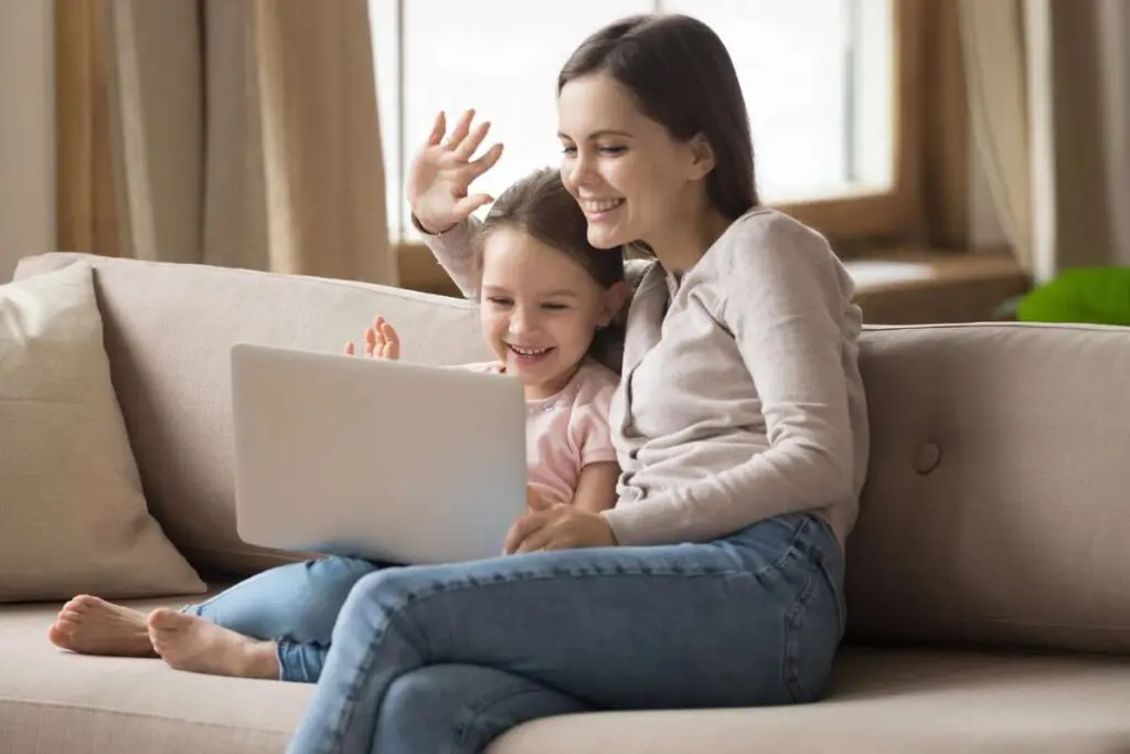 Smiling mom and little daughter talk on webcam using laptop.