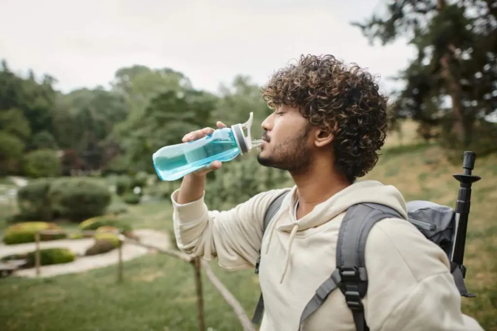 A man out in nature drinking water from his tumbler.