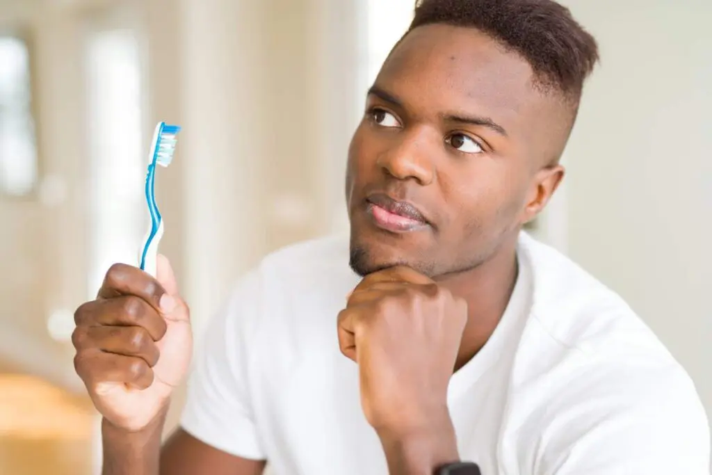 A man is deep in thought while holding his toothbrush.