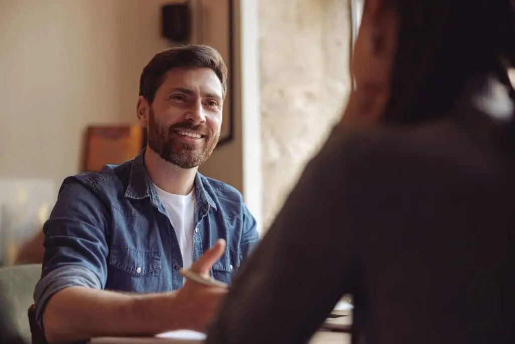 A man smiling to the woman seated across him.