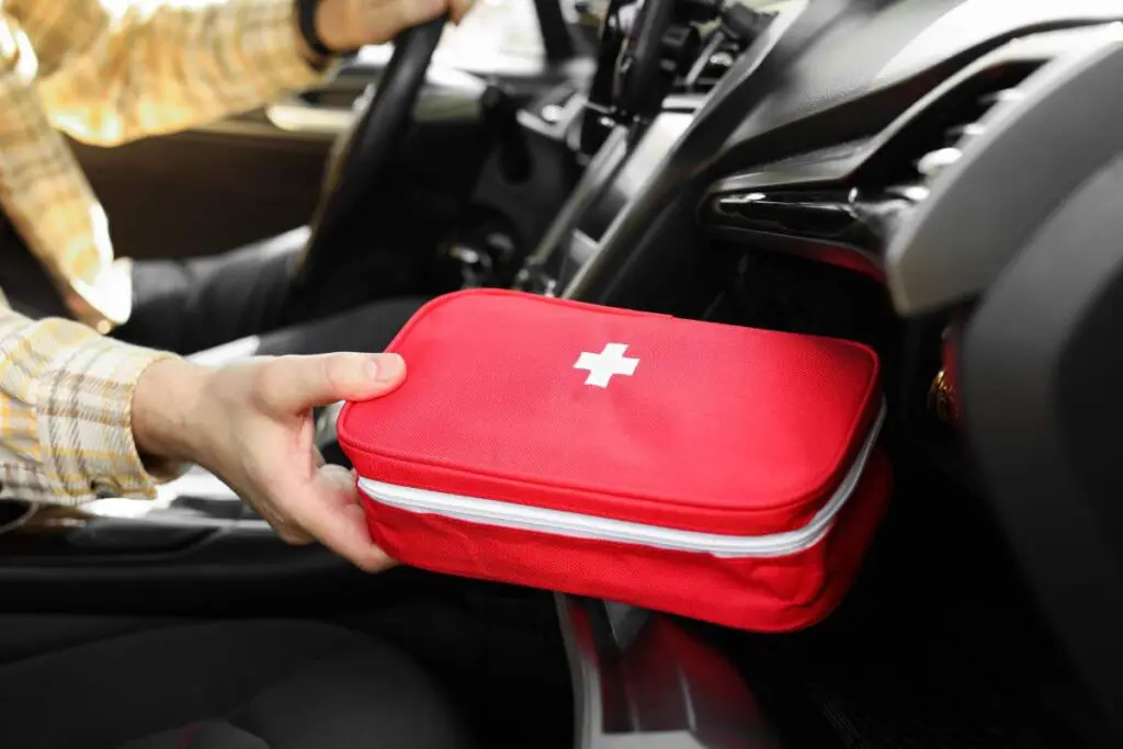 A person sitting in a vehicle holding a red first aid kit.