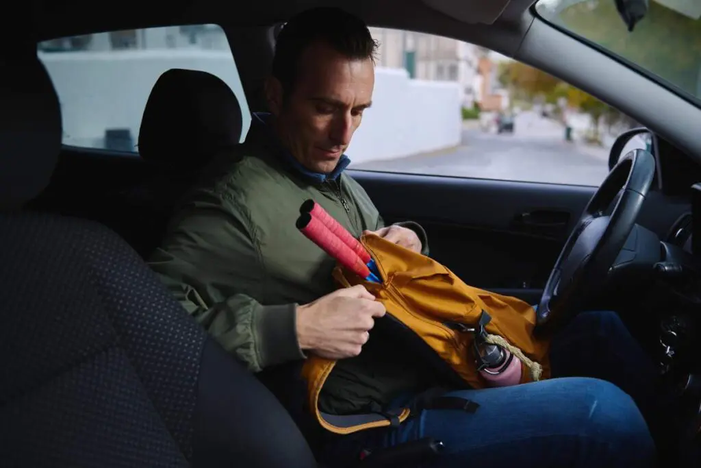 A man sitting in a car, looking at a backpack placed on his lap.