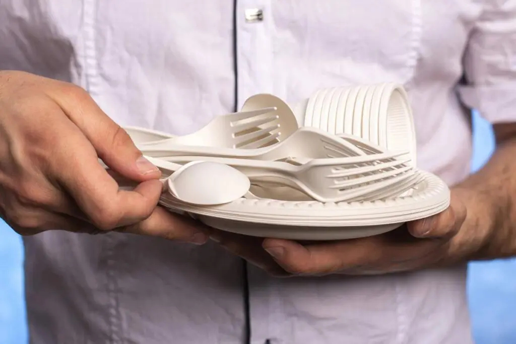 A man holds a plate filled with white plastic cutlery.