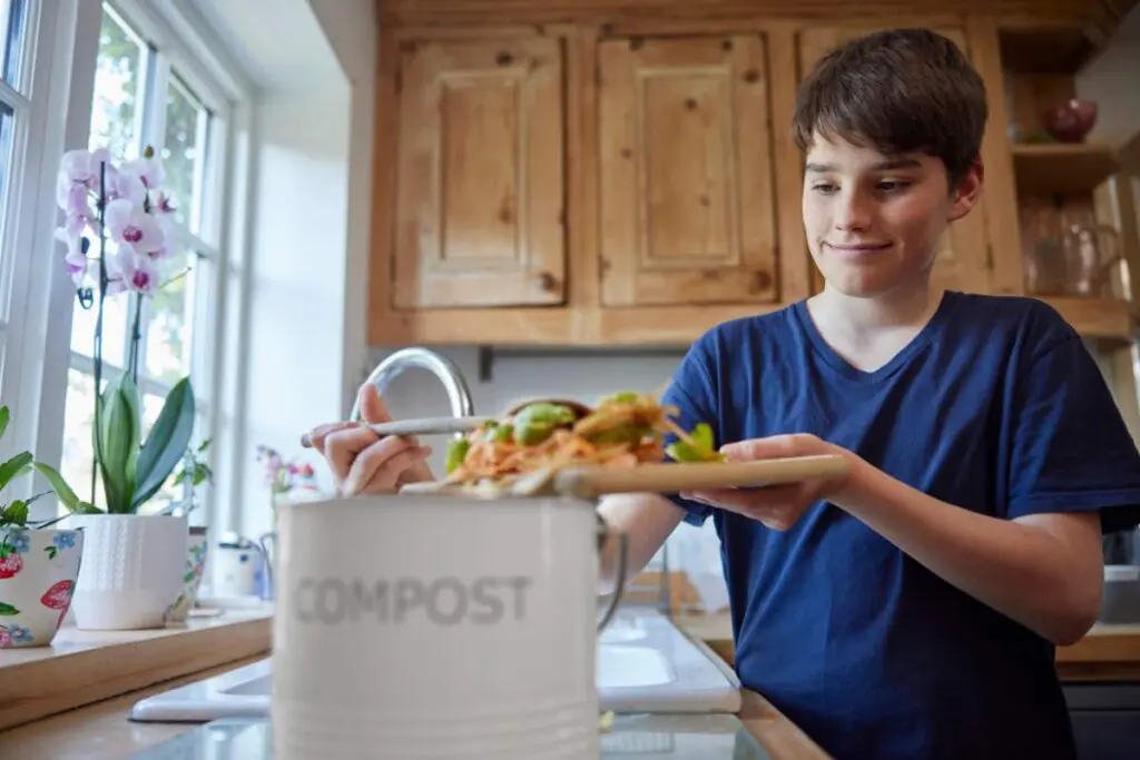 A boy stands in the kitchen, holding a container of food with a focused expression.