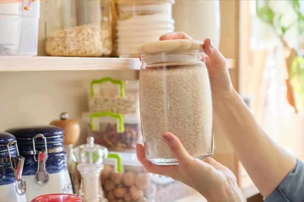 A close-up of a hand holding a glass jar filled with rice.