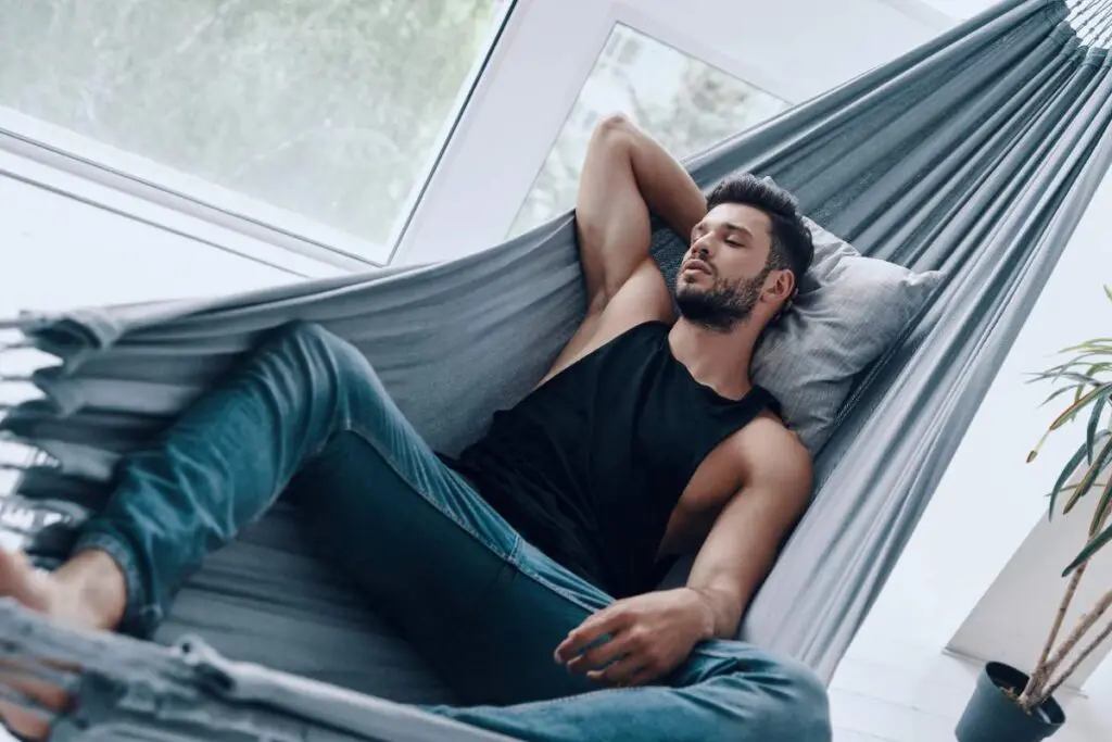 A man lying in a hammock indoors, with sunlight coming through a window.