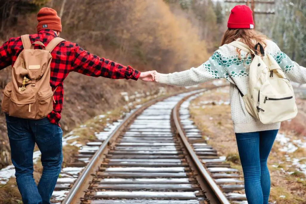 Two people standing on a railroad track, holding hands.