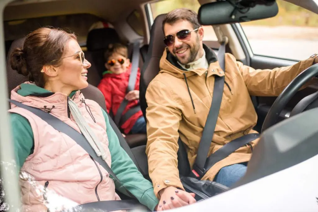 A man and woman sitting in a car with a child in a car seat.