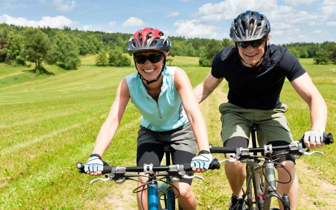 A man and woman riding bicycles on green grass, both wearing helmets.
