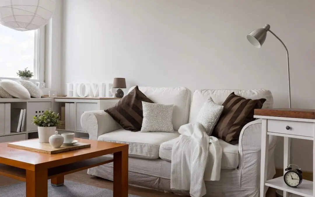A white couch is placed in a room featuring a coffee table, various pillows, and a vase.
