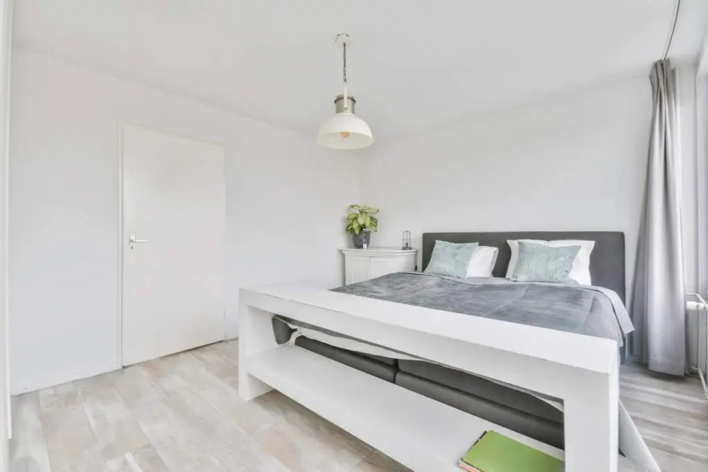 A white room featuring a bed with white bedding, a nightstand beside it.