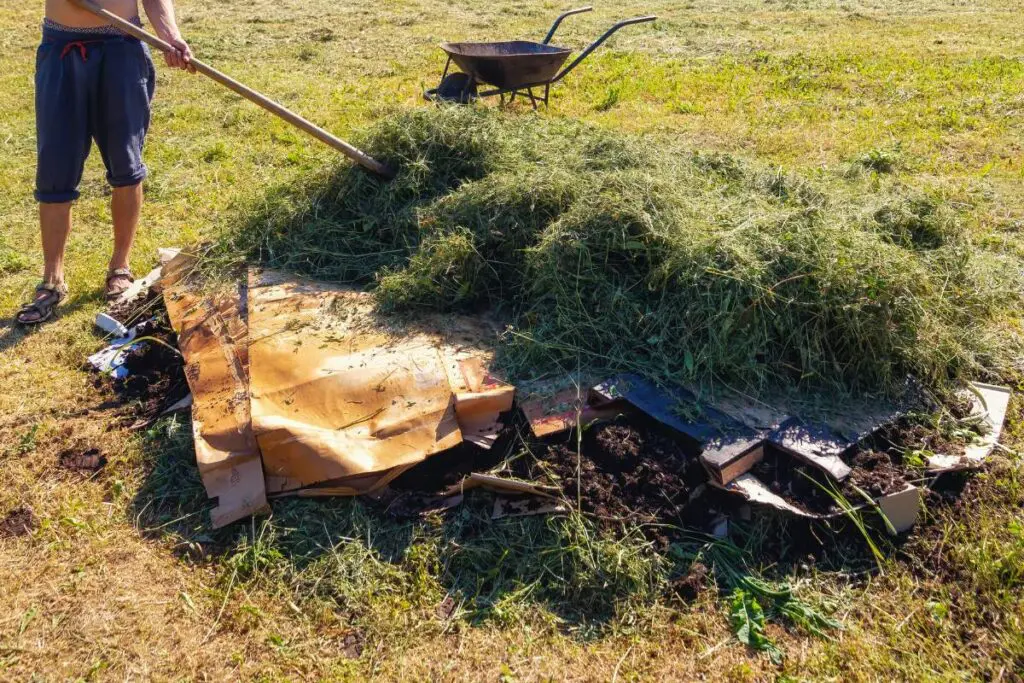 A person standing outdoors, holding a shovel over a large pile of grass.
