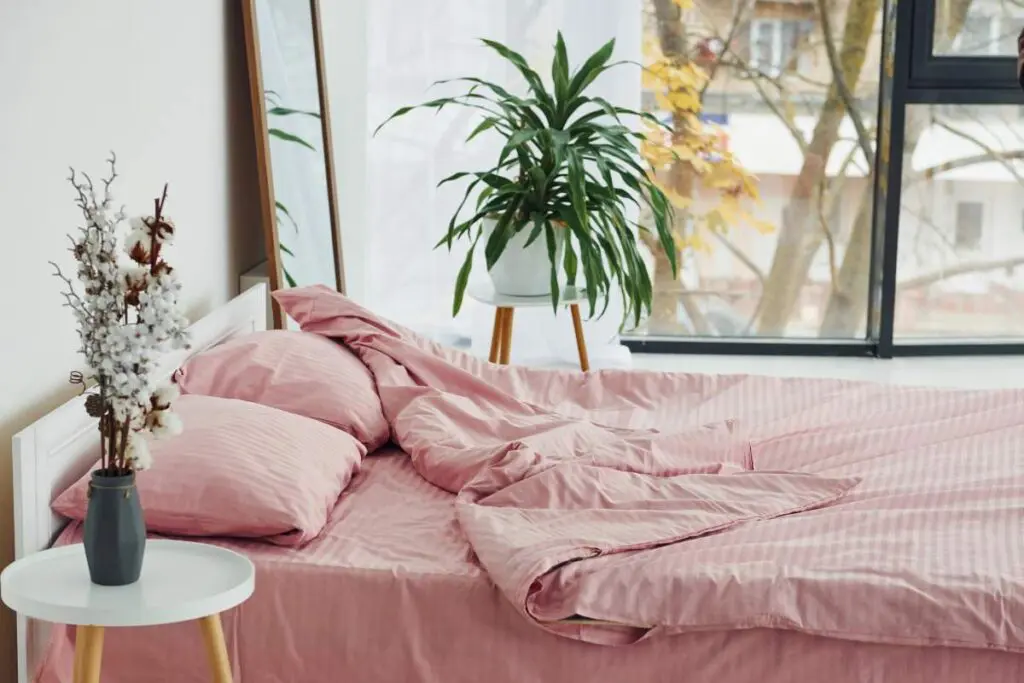 A pink bed with colorful linens and decorative pillow.