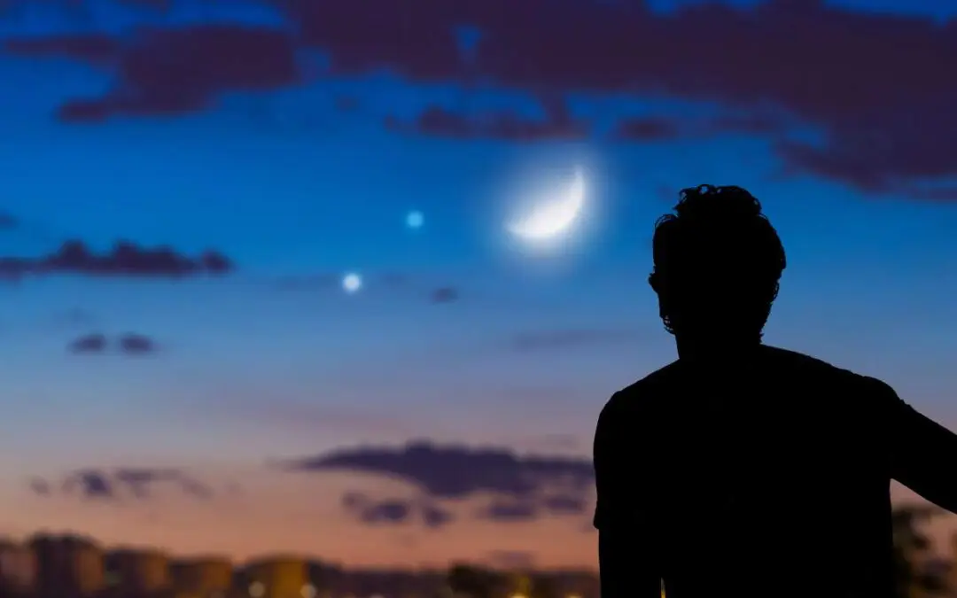 A silhouette of a man gazing at the moon against a backdrop of clouds during sunset.