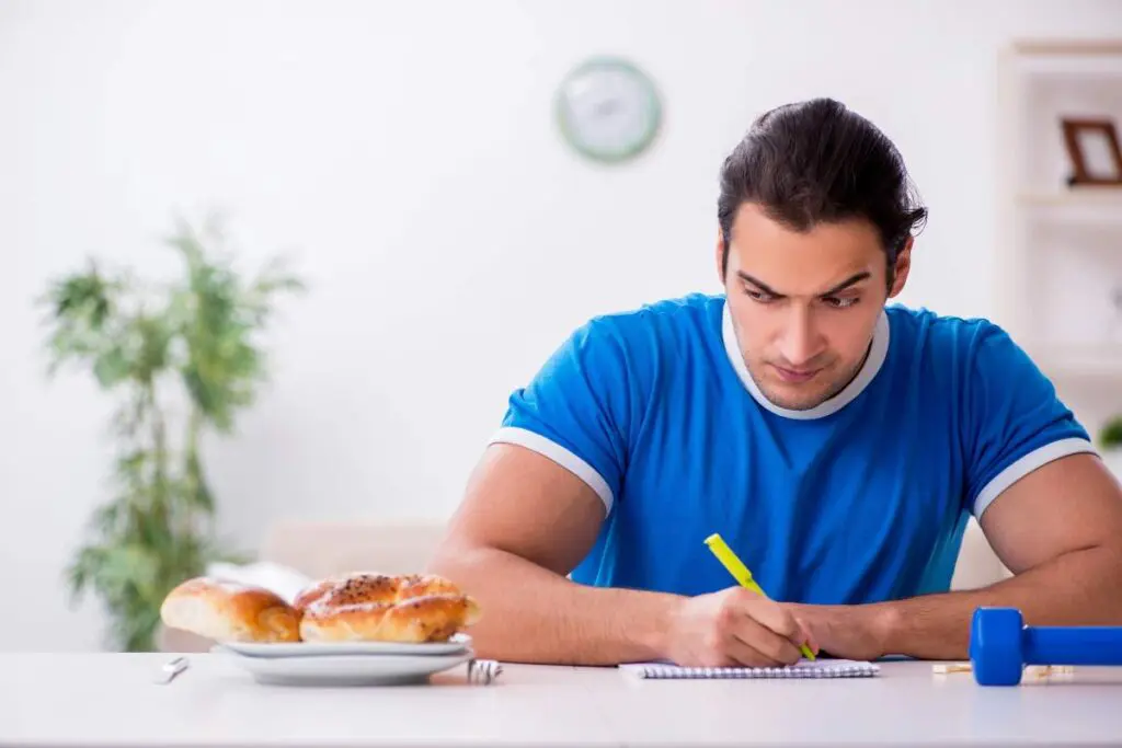 A man sitting at a table indoors, wearing casual clothing, writing in a notebook.