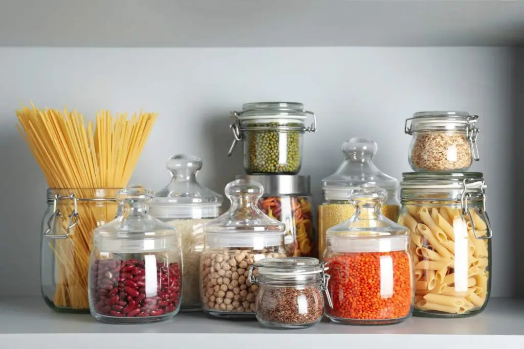 A collection of glass jars filled with various types of pasta, grains, and legumes, neatly arranged on a shelf.