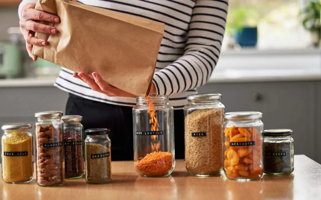 A person in a striped shirt is pouring contents from a brown paper bag into a glass jar.