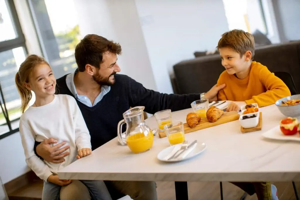 A father sitting at a table with his two children, enjoying breakfast together.