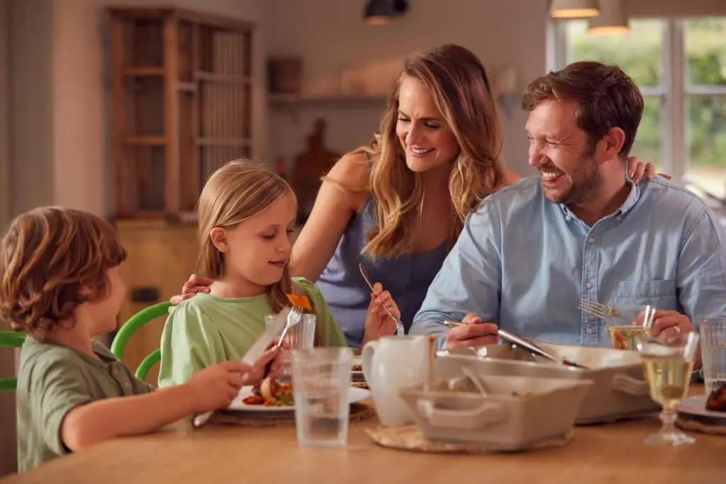 A family enjoying a meal together at a dining table, with two children and two adults sharing food and smiles.