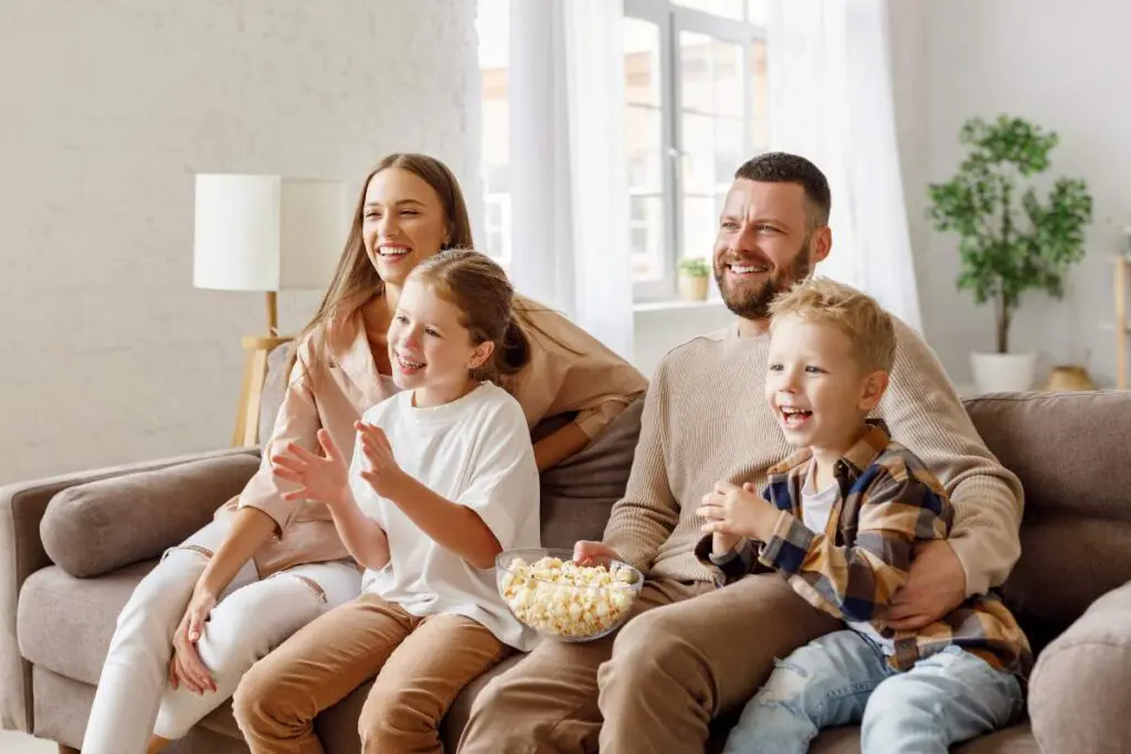 A happy family sitting on a couch, enjoying popcorn and watching something entertaining together.