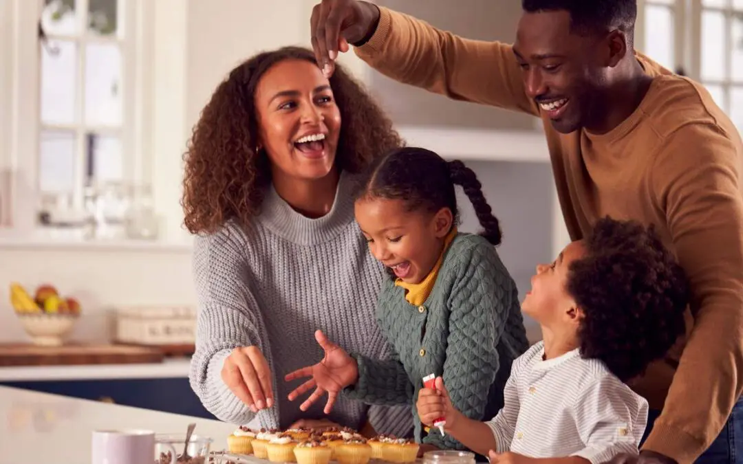 A happy family in a kitchen, with a mother and father playfully decorating cupcakes with their children.