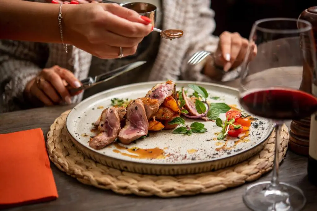 A plate of gourmet food featuring sliced meat, roasted vegetables, and garnishes.