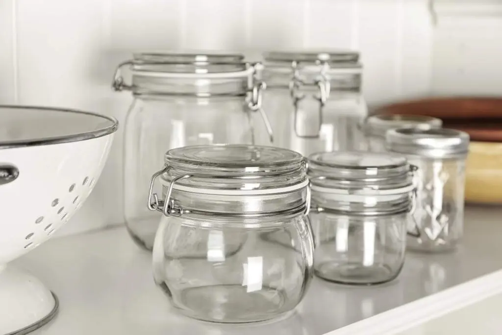 A collection of clear glass jars with metal lids, displayed on a white shelf.