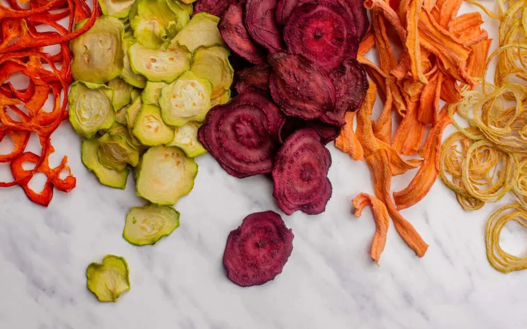 A variety of colorful sliced vegetables including red, green, and orange, arranged on a marble surface.