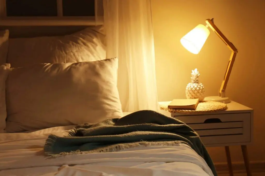 A cozy bedroom scene featuring a bed with white pillows, a bedside table with a lamp illuminating the space.