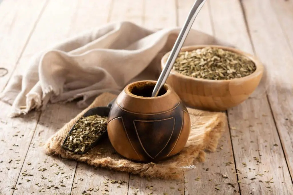 A wooden gourd (mate) sits on a rustic wooden surface with a metal straw inserted.