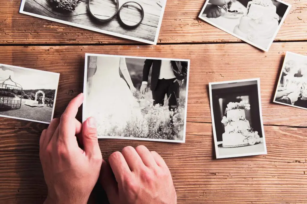 A collection of black and white photographs laid out on a wooden surface, with a pair of hands holding one photo.