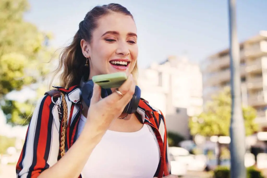 A young woman with long hair is outdoors, smiling while talking on a smartphone.