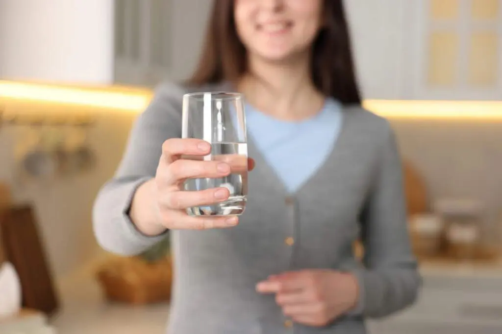A woman in a gray cardigan holding a glass of water, smiling.