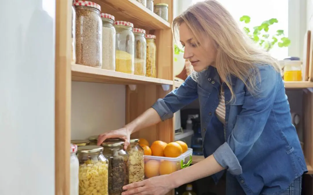 A woman organizing jars of food on shelves in a kitchen or pantry.