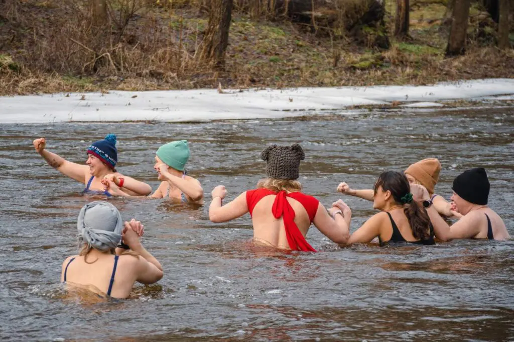 A group of women swimming in a river, wearing swimwear and winter hats, with some ice visible on the shore.
