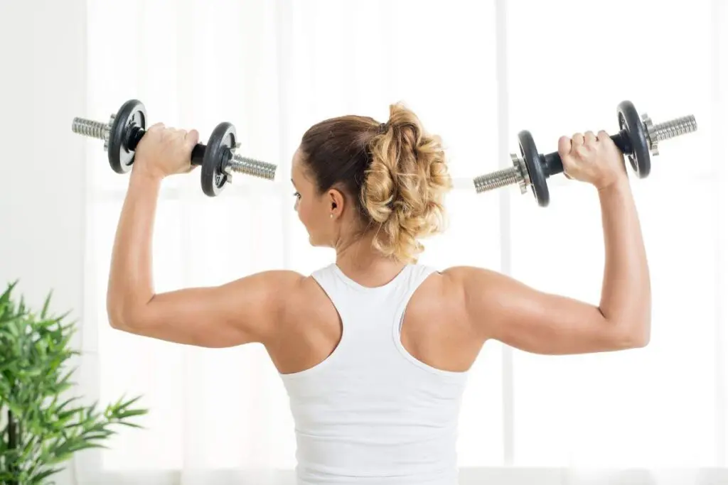 A woman with a ponytail is lifting dumbbells in an indoor setting, focusing on her upper body workout.