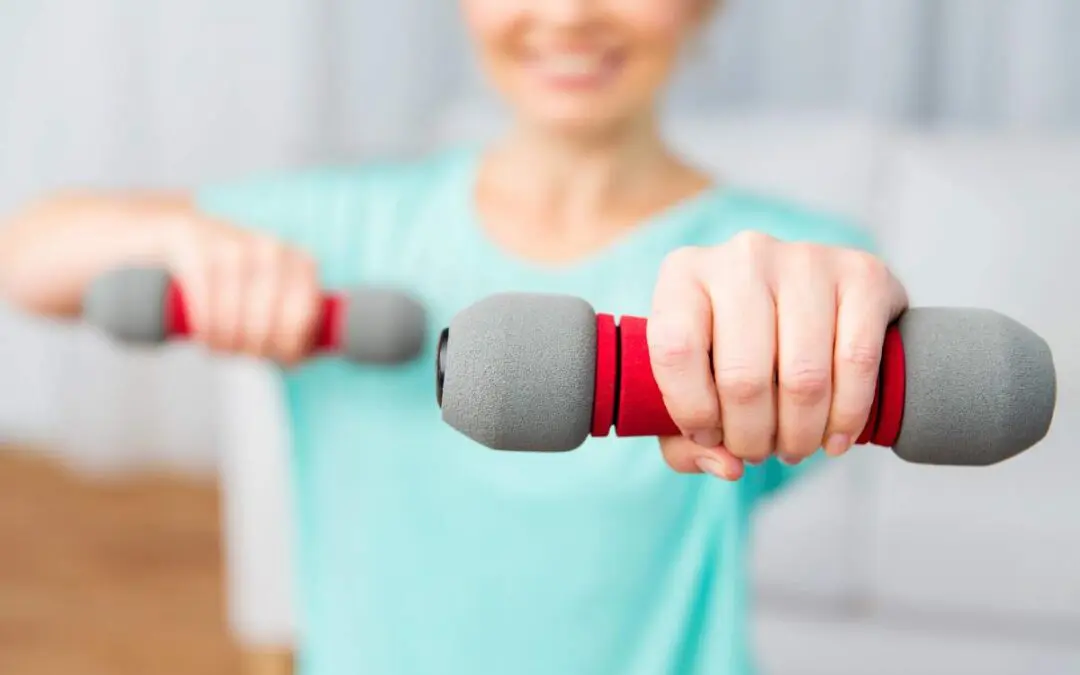 A person holds two red and grey dumbbells in a fitness setting, appearing to engage in exercise.