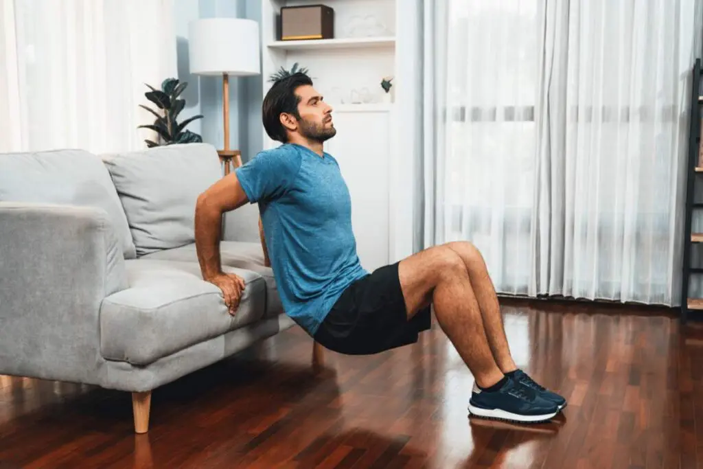 A man performing tricep dips on a couch in a living room setting.