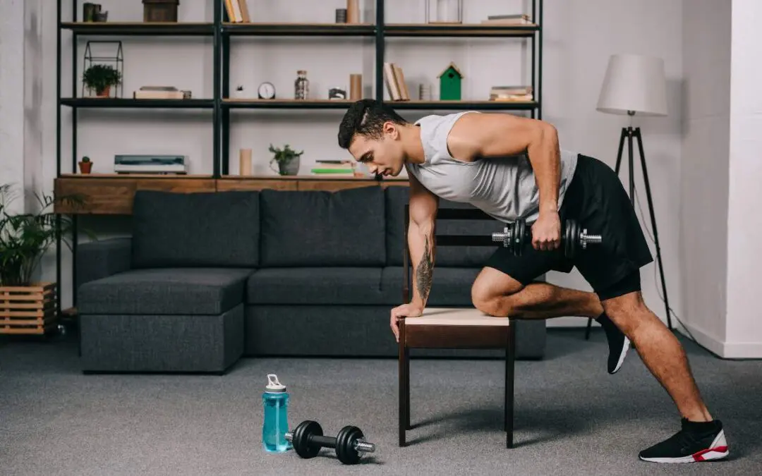 A man performing a bent-over row exercise with a dumbbell while using a bench for support, in a living room setting with workout gear nearby.
