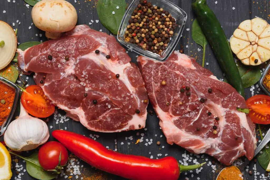 Raw pork chops surrounded by various spices, vegetables, and herbs.