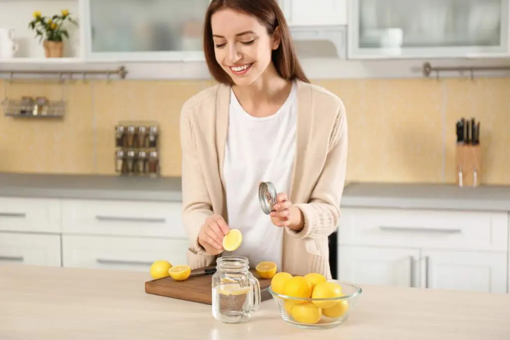 A woman slices lemons in a modern kitchen, preparing to add them to a jar of water.