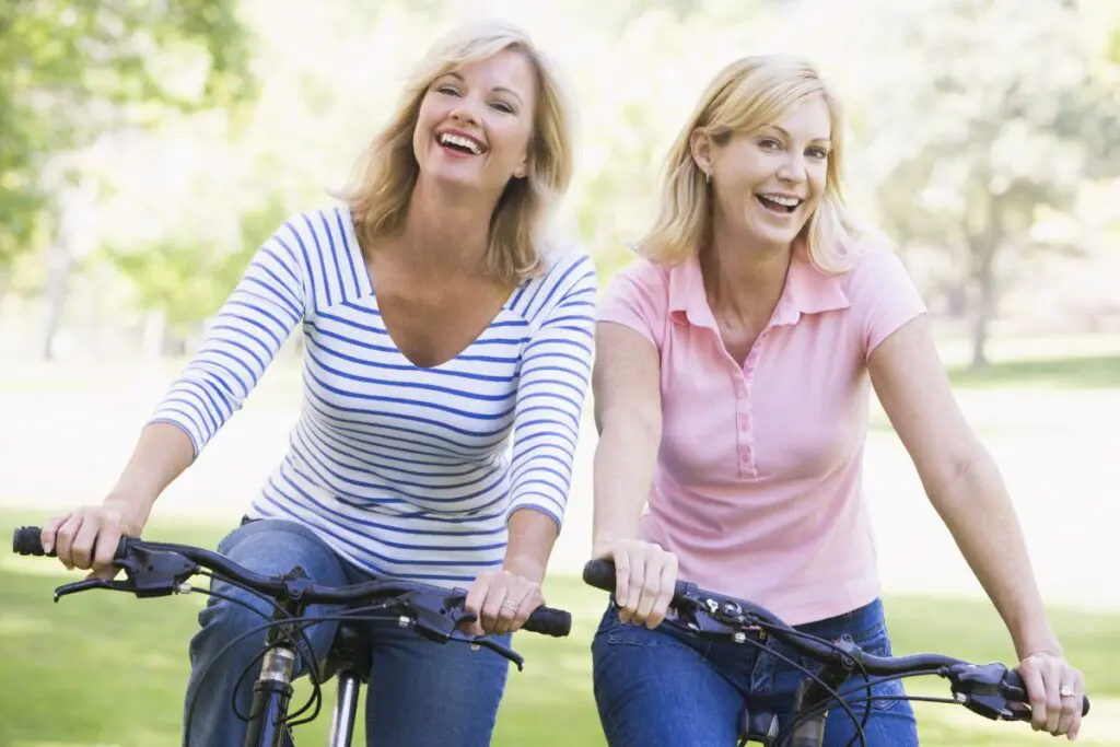 Two women riding bicycles and smiling in a park.
