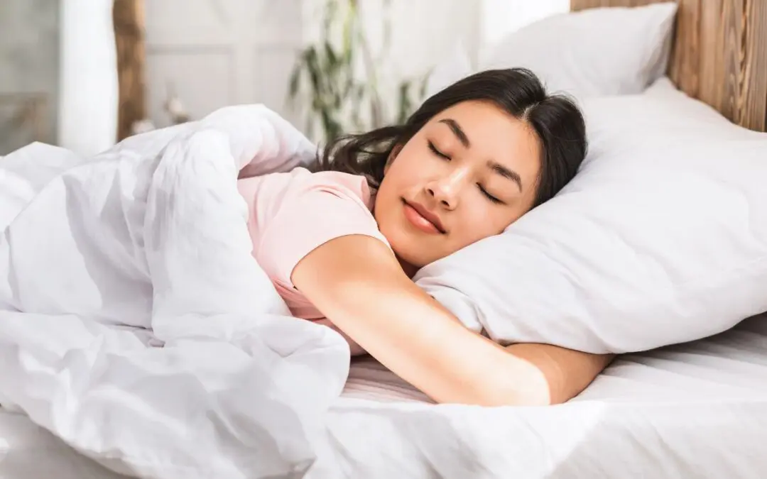 A young woman peacefully sleeping in bed, covered with white blankets, in a softly lit room.